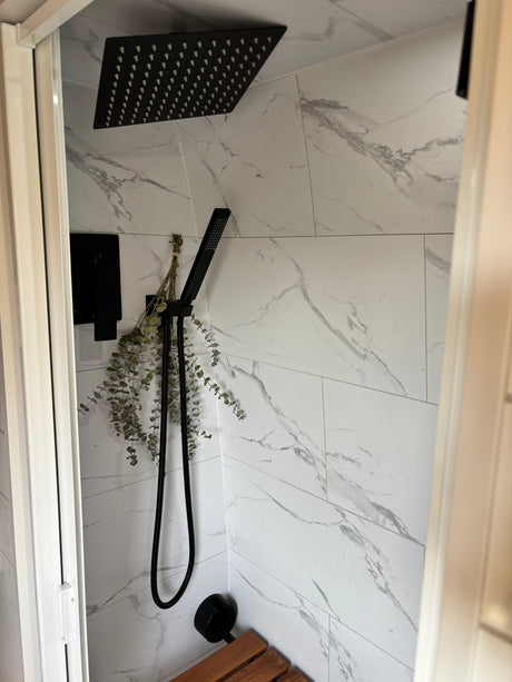 Modern RV rental shower: black fixtures, elegant marble-look tiles, and dried eucalyptus for a refreshing experience.