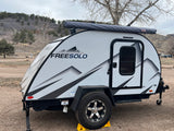 White "FREESOLO" teardrop RV rental parked at a mountain campsite, ready for outdoor adventure.