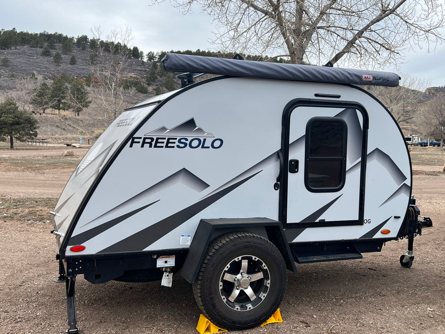 White "FREESOLO" teardrop RV rental parked at a mountain campsite, ready for outdoor adventure.