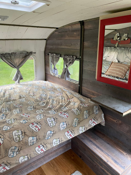 Relax in this cozy rv rental bedroom, featuring a "Happy Camper" comforter, rustic wood walls, and bright windows.