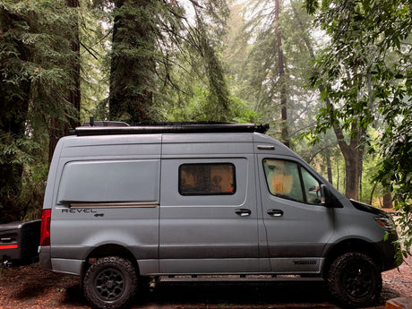 Explore misty redwoods in this grey Winnebago Revel rv rental van, parked amidst tall trees.