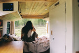 Cozy interior of an RV rental with a person relaxing on the bed, enjoying a serene forest view.