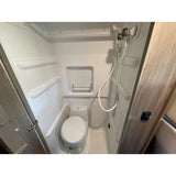 RV rental's compact wet bath: white interior with a toilet, shower, and small shelf. Ideal for travel & camping.