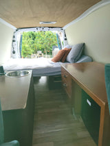 Cozy RV rental interior with bed, sink, desk, and outdoor view. Perfect for mobile living in this camper van.