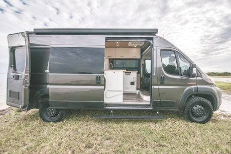 Grey camper van, side open revealing its custom interior, parked oceanside. Perfect for an rv rental adventure.