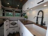 Inside a stylish RV rental camper van: white kitchen with a farm sink, wood counters, and gray bedding for a comfortable road trip.