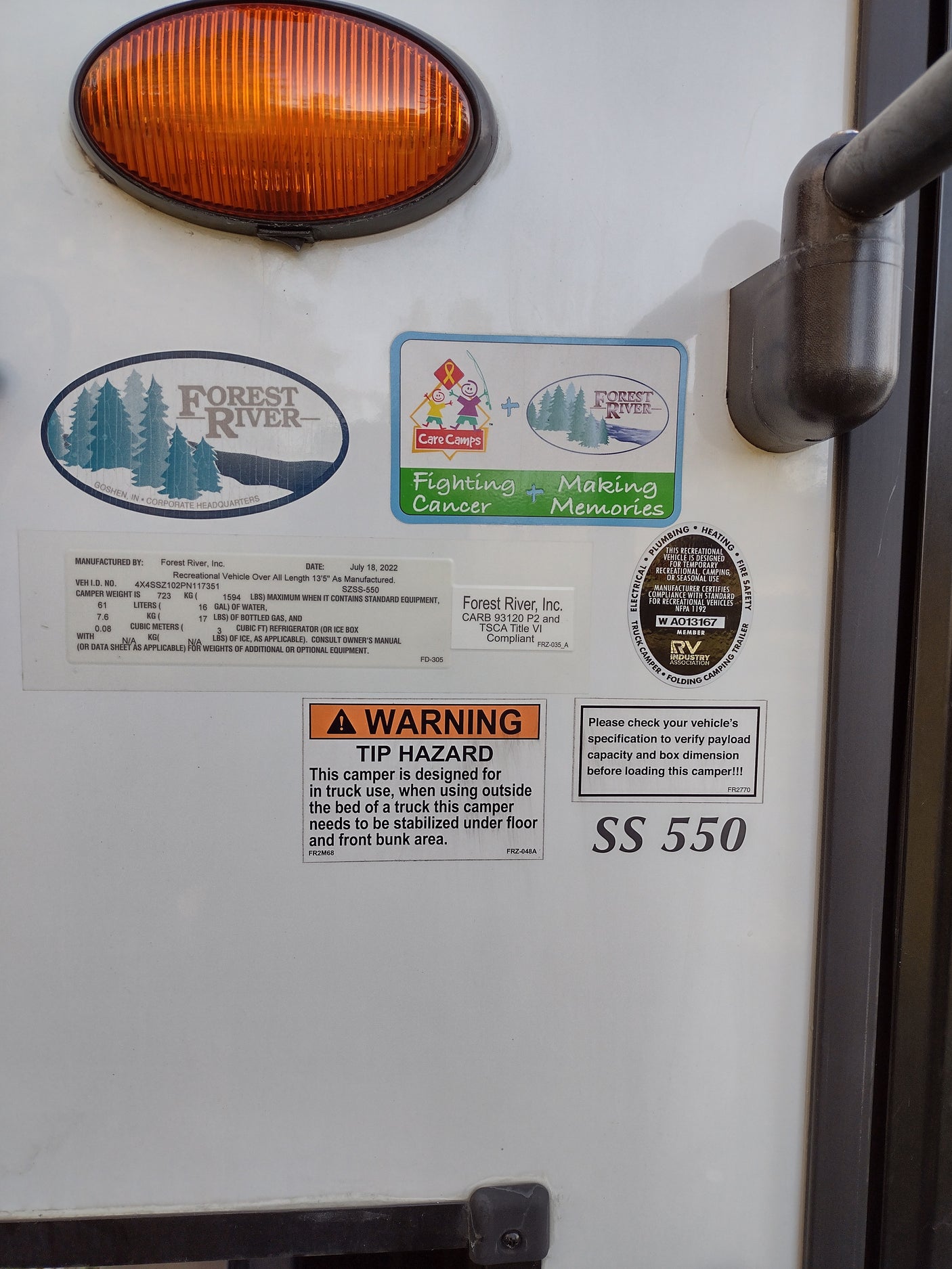 Close-up of an RV rental camper side, showing manufacturing labels, weight specs, and hazard warnings. Model SS 550.