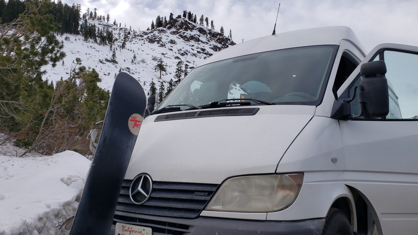Mercedes Sprinter RV rental van with a snowboard, parked in a snowy mountain setting, ready for winter adventure.