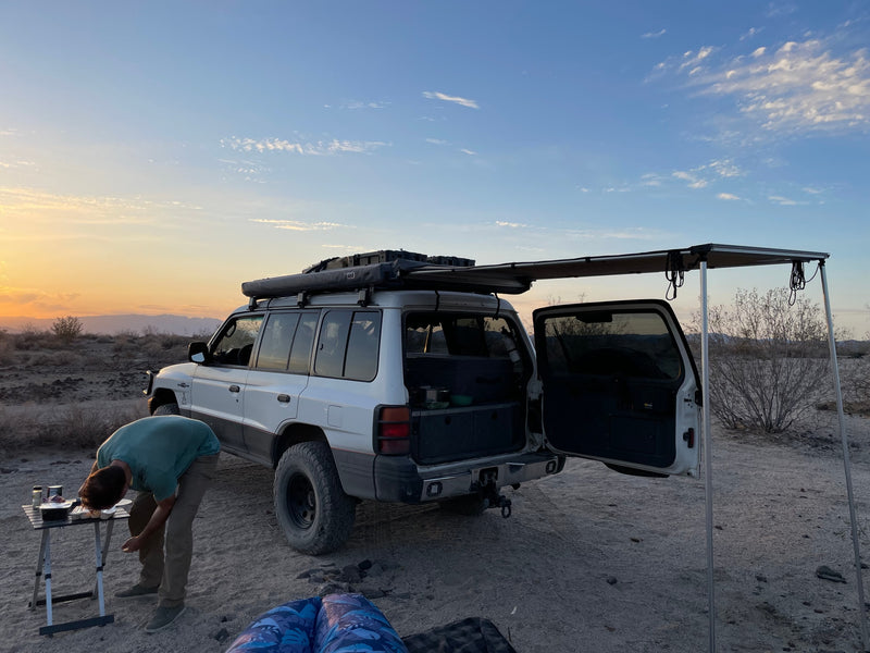 Experience overlanding with an SUV setup like an RV rental. Desert camp at sunset, person preparing food by the vehicle. — photo 3