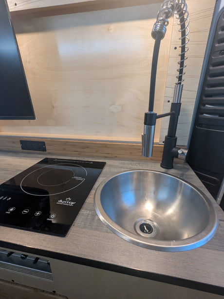 Compact kitchen in an RV rental, featuring a Duxtop induction cooktop and a pull-down faucet over a stainless steel sink.