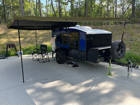 A compact blue camper trailer with a large awning parked on a paved campsite, ready for an RV rental outdoor adventure.