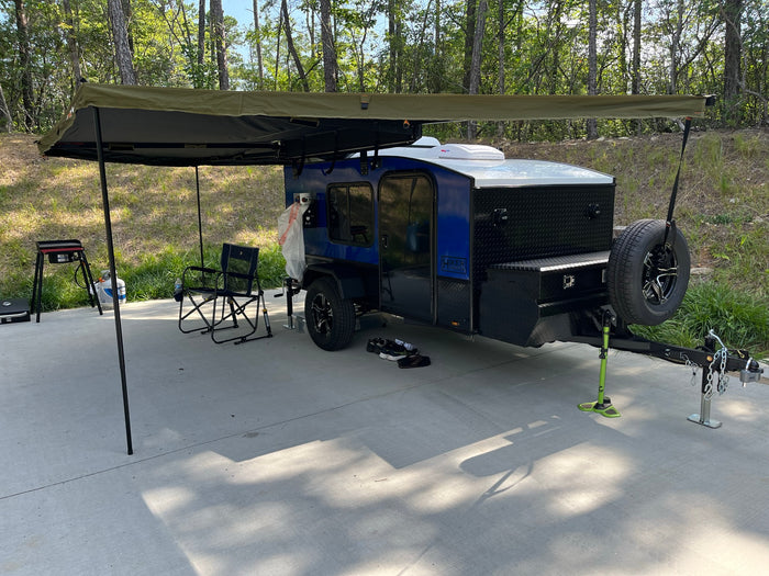 A compact blue camper trailer with a large awning parked on a paved campsite, ready for an RV rental outdoor adventure.