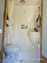 A functional rv rental bathroom featuring a shower, toilet on a platform, compact sink, and essential toiletries.