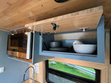 Functional RV kitchen with overhead microwave and open gray cabinet, neatly storing bowls and plates, ideal for your rv rental trip.