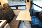 An RV rental interior features two black leather rear seats, a light wood table, and the front passenger seat.
