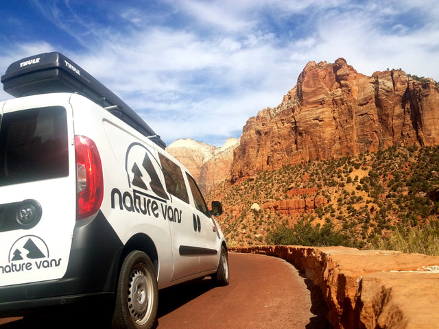 Nature Vans RV rental with Thule box on scenic red rock road. Ideal for park adventures under blue skies.