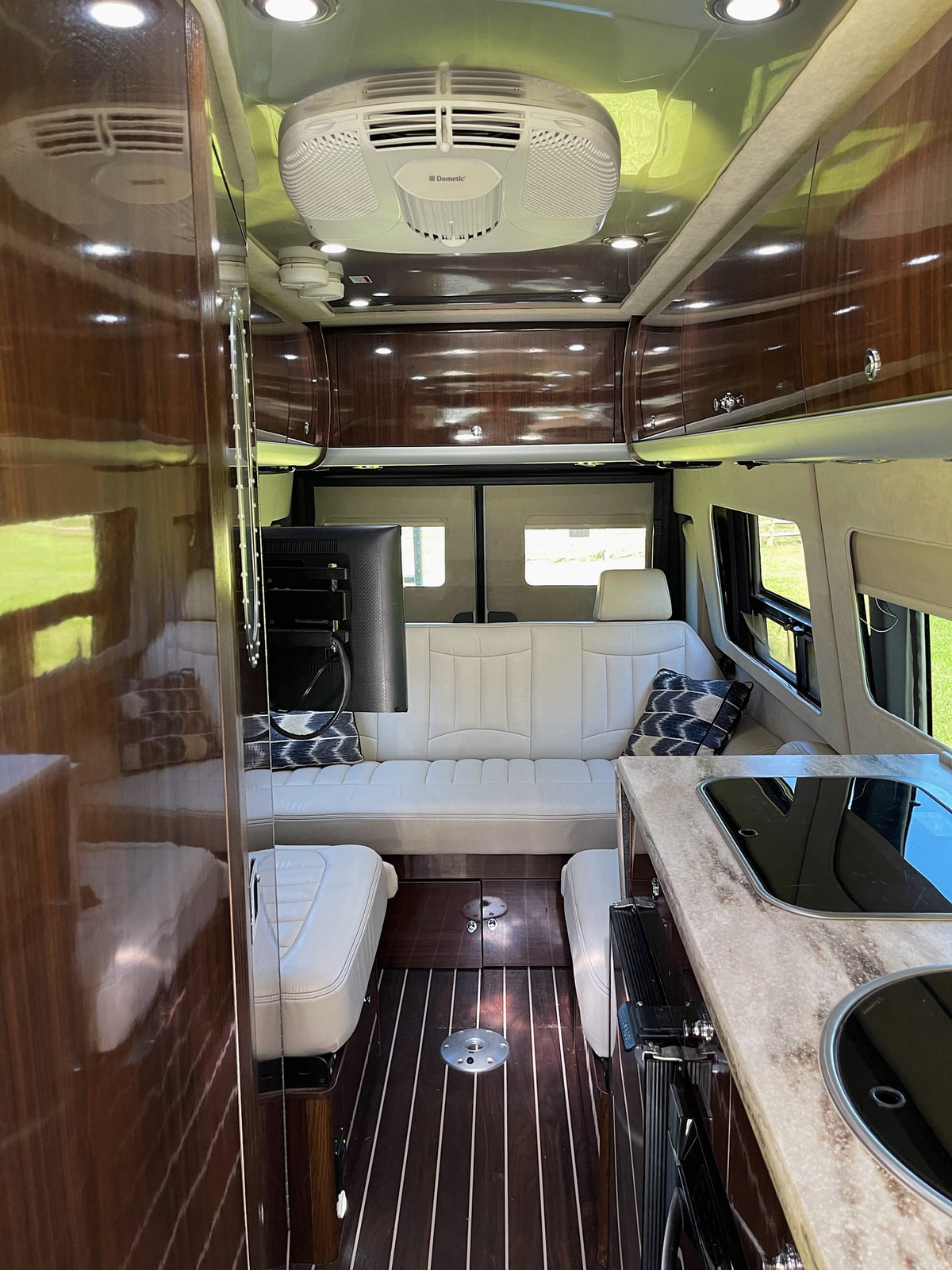 Step inside this premium RV rental: sleek interior with white leather seating, kitchen, wood flooring, & TV. — photo 9