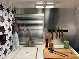 Efficient RV rental kitchen featuring a sink, magnetic knife strip, tiled backsplash, and compact counter space.