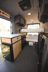 This RV rental camper van interior features a compact kitchen, bunk beds, and clever overhead storage, creating an efficient mobile living space.