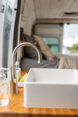 Cozy RV rental kitchen with a modern sink, faucet, and wooden counter, perfect for mobile adventures.
