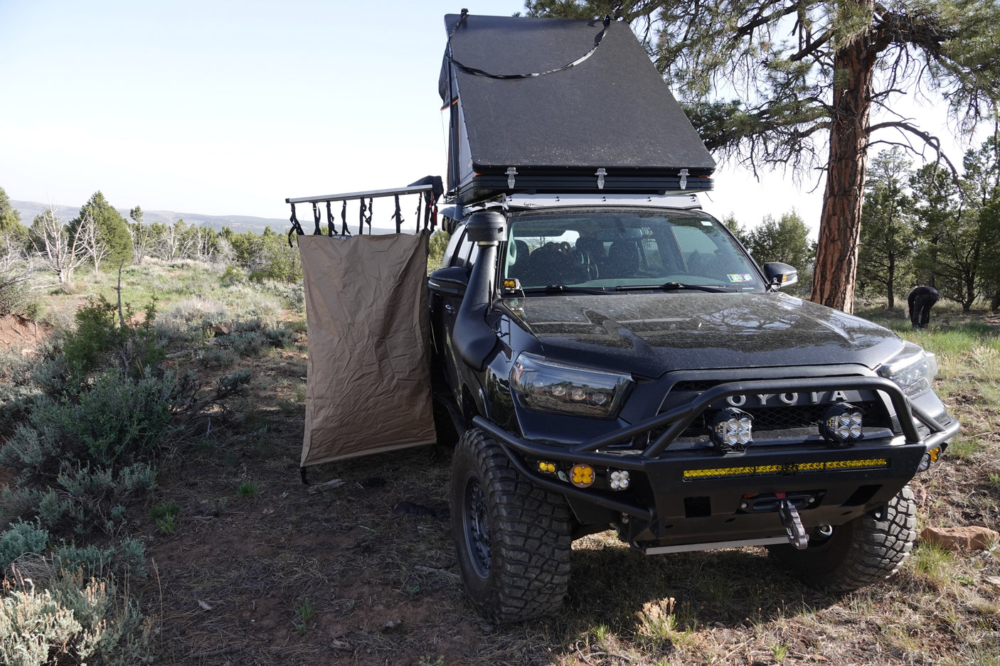 A rugged black overlanding truck with a rooftop tent and side privacy shelter, perfect for your next rv rental style adventure.