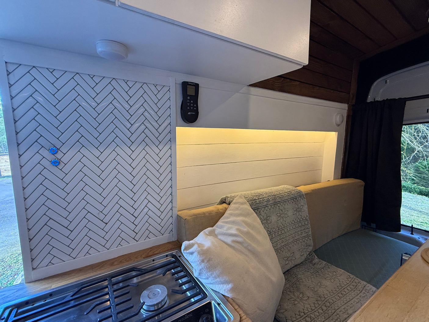 This RV rental's kitchen features white herringbone tiles, a Dometic stove, and a cozy lounge with warm light.