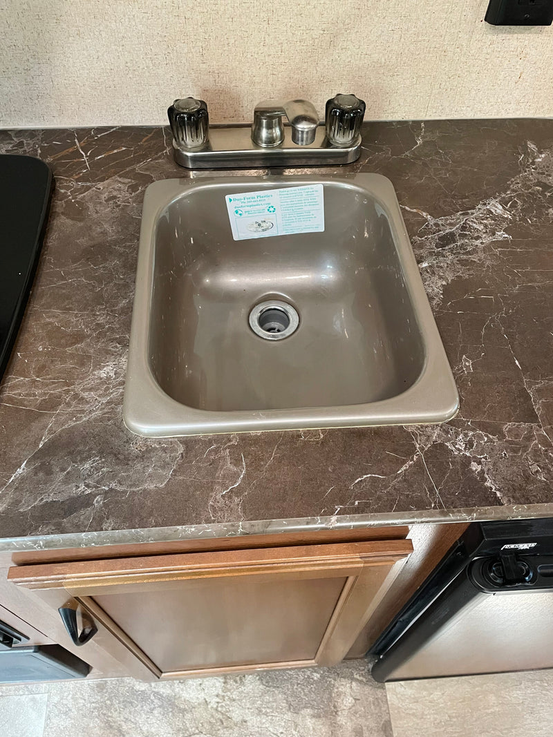 RV rental kitchen: small sink, faucet, dark marbled countertop, and wood cabinetry below. — photo 9
