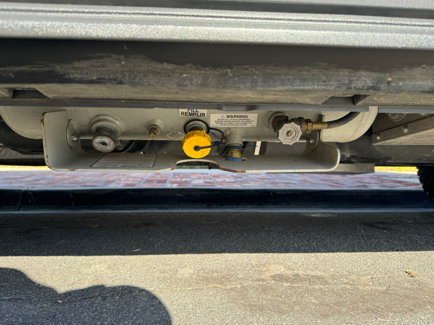 RV rental undercarriage showing LP-gas propane tank with fill port, pressure gauge, and warning label for safe operation.