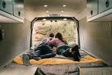 Relaxing in a cozy RV rental, two people enjoy the outdoor view from their camper van bed.