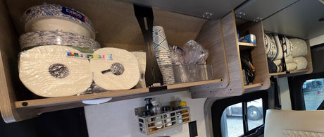 RV rental overhead cabinets neatly stocked with paper plates, cups, paper towels, and pillows, showcasing efficient travel storage.