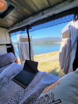 Inside an RV rental: Bed with a laptop, offering a scenic lake and mountain view through screened doors for remote work.