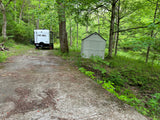 NOBO **RV rental** parked on a forest clearing beside a shed, with a paved approach. Ideal for a nature escape.