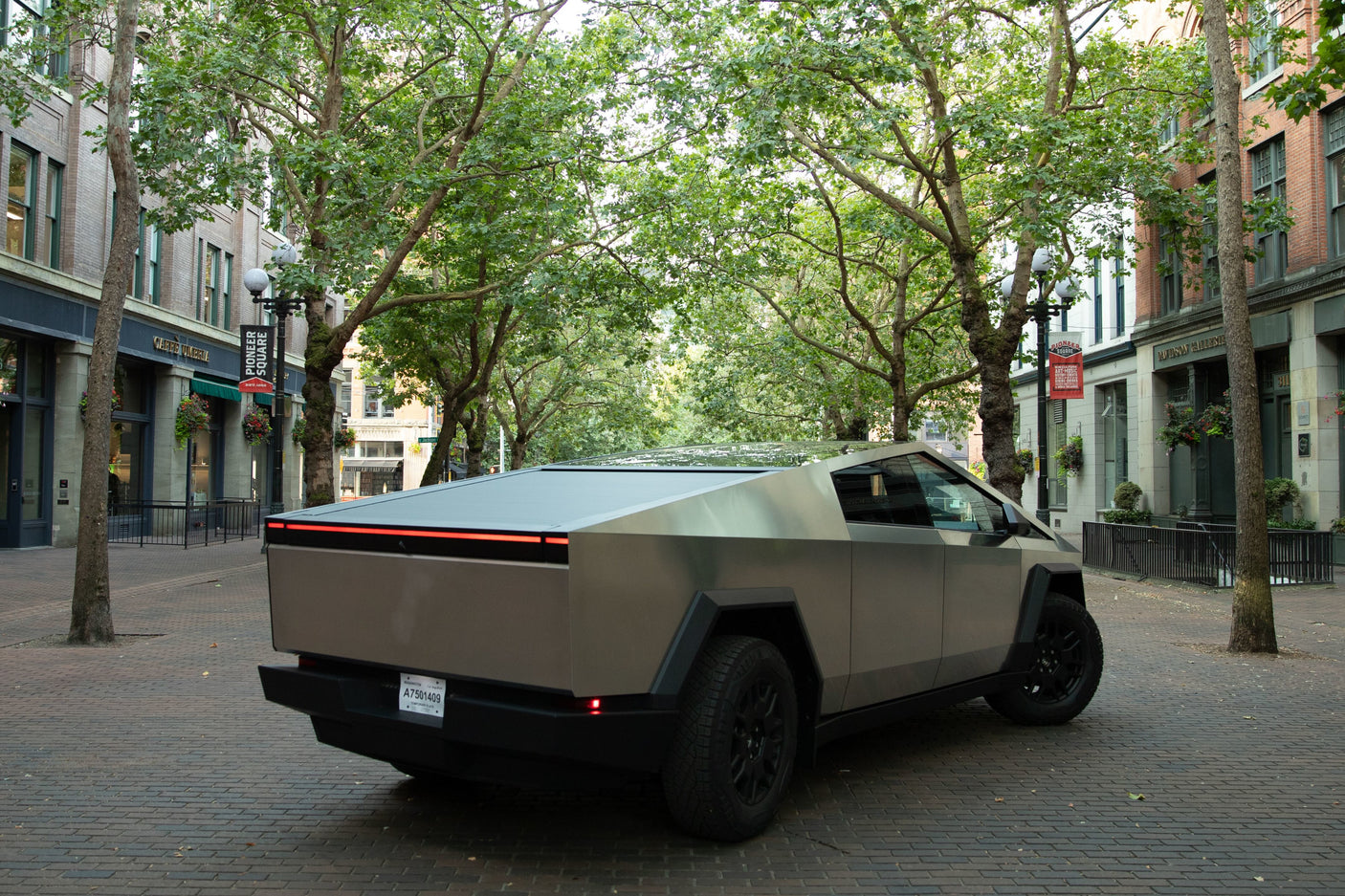 A grey Tesla Cybertruck on an urban brick street. Its unique design could suit an rv rental adventure. Trees & buildings.