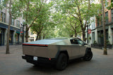 A grey Tesla Cybertruck on an urban brick street. Its unique design could suit an rv rental adventure. Trees & buildings.