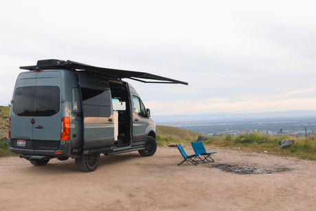 This Storyteller Overland Sprinter van is a perfect RV rental, parked on a scenic overlook with chairs and a fire pit.
