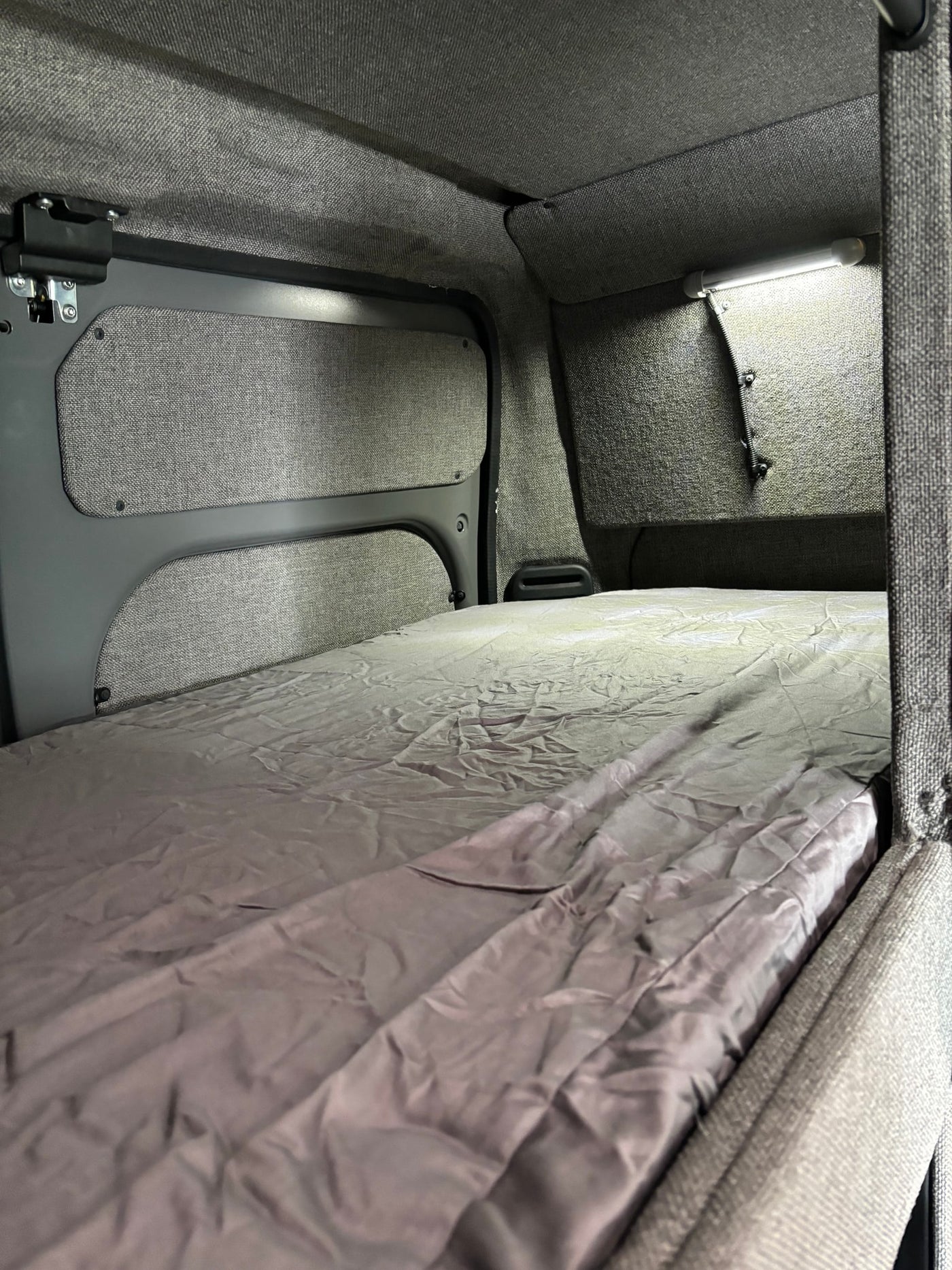 Step into comfort: an RV rental sleeping area featuring a neatly made bed, grey upholstered walls, and practical LED lighting. — photo 7