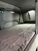 Step into comfort: an RV rental sleeping area featuring a neatly made bed, grey upholstered walls, and practical LED lighting.