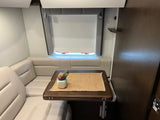 This RV rental features a comfortable dinette: plush seating, wooden table with decor, and adjustable window blinds.