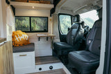 Inside a modern RV rental: a bright living space with a scenic lake view, comfy "Happy" pillow, and driver's cab.