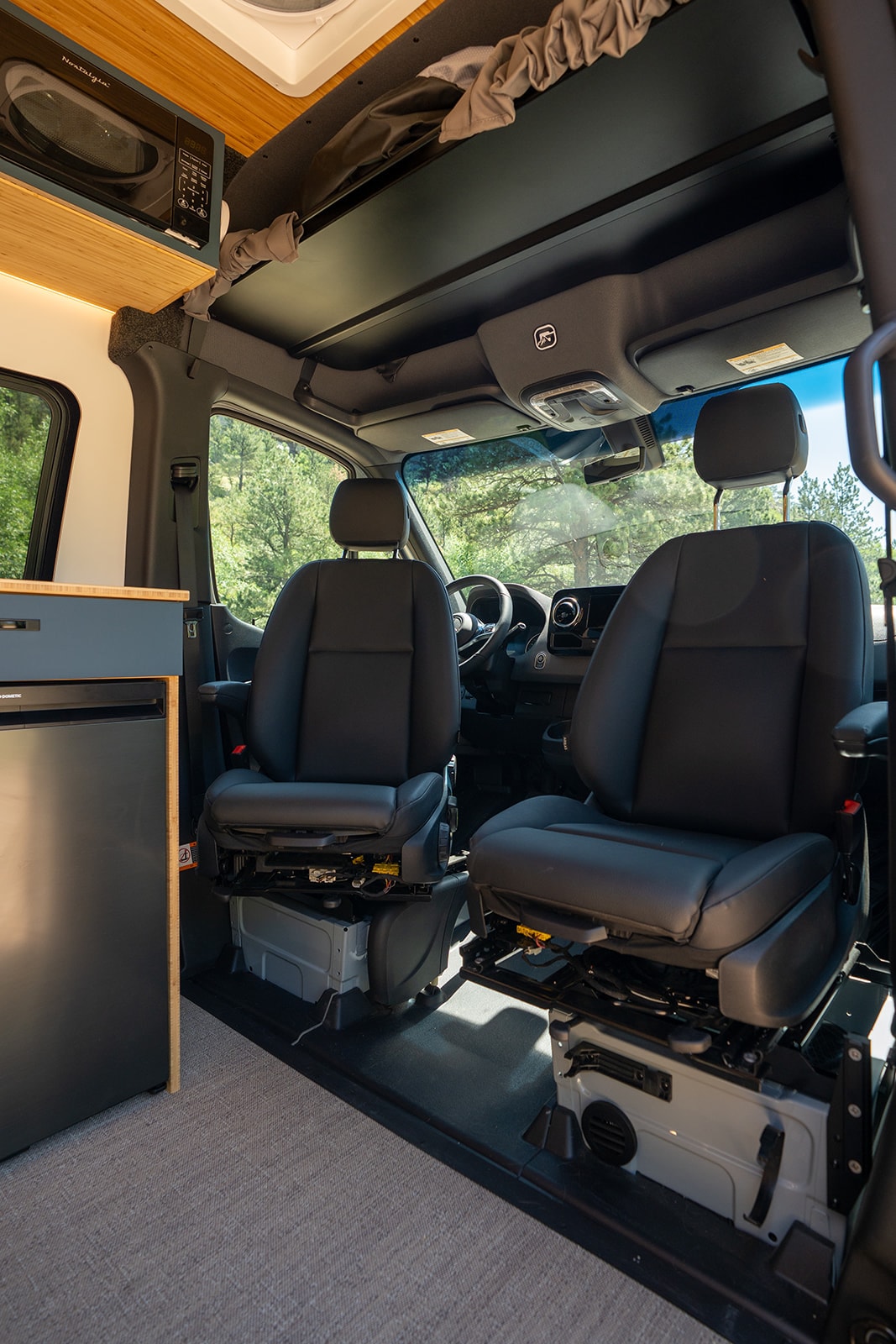 Modern rv rental interior: Driver's view with swivel seats, overhead storage, microwave, and fridge. — photo 12