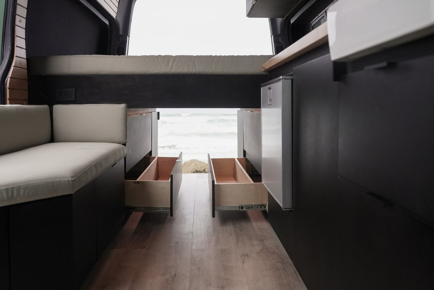 Modern RV rental interior with open back, showing beach view, bench seating, and pull-out storage drawers. — photo 10