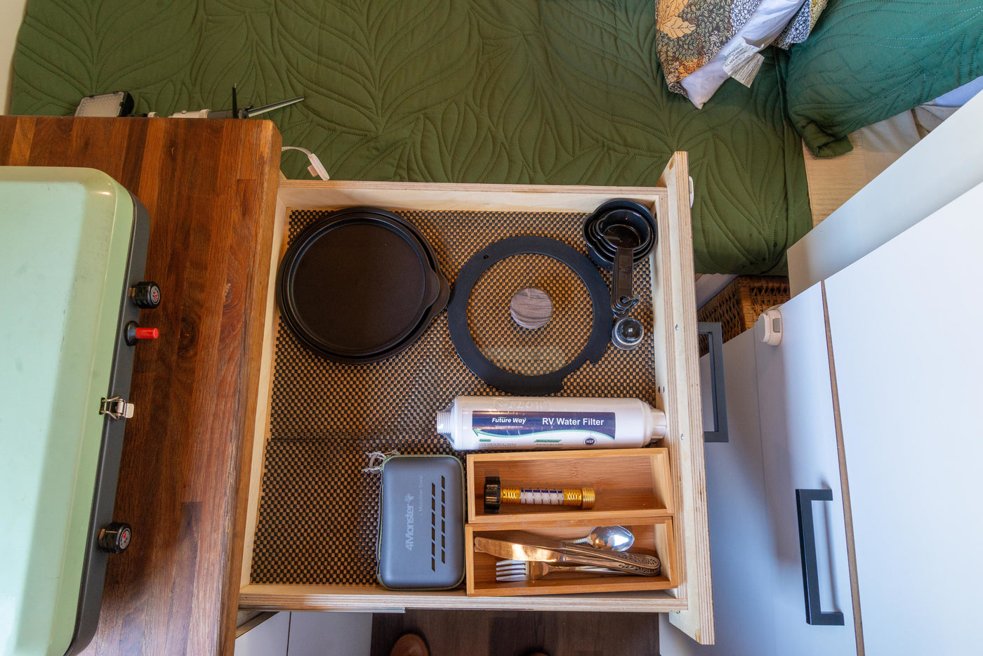 Inside an RV rental, a well-organized kitchen drawer holds a cast iron pan, RV water filter, measuring cups, and utensils. — photo 16