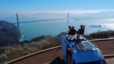 Golden Gate Bridge view from an RV rental. Two people relax on van's rooftop at a scenic overlook.