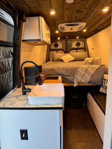 Cozy RV rental interior with bed, kitchen, and wood ceiling. Perfect for compact living on the road.