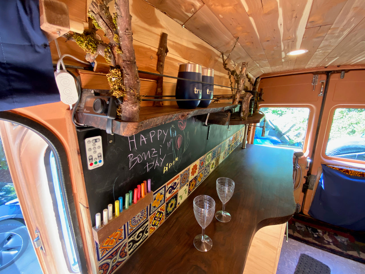 This unique RV rental boasts a custom wood interior with a rustic bar, chalkboard, colorful tiles, and two wine glasses.