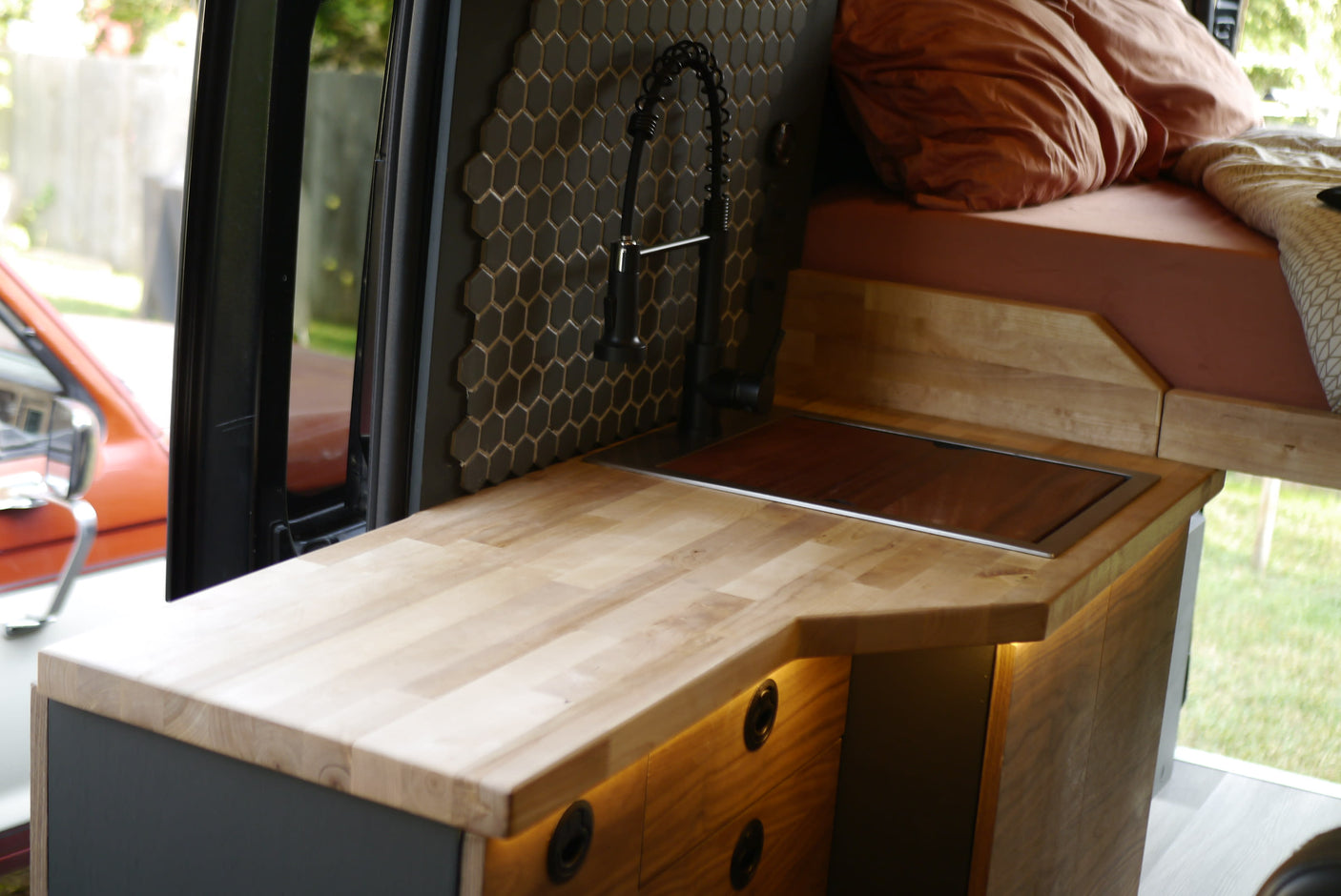 RV rental with modern camper van interior, featuring a compact kitchen with wood counters, sink, and tiled backsplash, plus a cozy bed area.