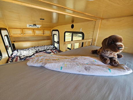 Cozy RV rental interior featuring two comfortable beds, light wood paneling, and a brown stuffed dog.