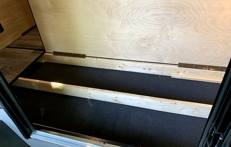 RV rental: Under-bed storage area revealed by a lifted wooden panel, showing support beams on a black floor. — photo 16