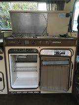 RV rental interior: A Westfalia camper kitchen with an open Dometic refrigerator, freezer, and gas stove.