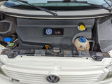 Volkswagen V6 engine bay of an RV rental, showing coolant, oil, and brake fluid reservoirs for maintenance.